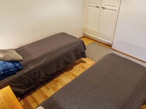Ein kleines Zimmer mit zwei Einzelbetten, Holzboden und einem weißen Kleiderschrank.