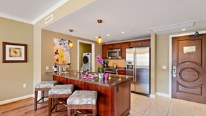 A kitchen with a central island, wooden cabinets, stainless steel appliances, and a bar stool seating area.