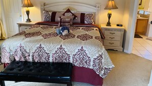 A neatly made bed with a patterned bedspread, two bedside lamps, a bedside clock, and a small bedside table.