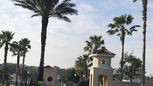 A gated entrance with palm trees and a small tower-like structure with a tiled roof.