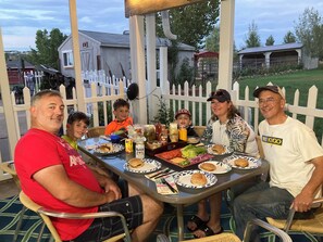 Uma família jantando ao ar livre numa mesa com vários pratos.