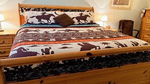 Uma cama com colcha estampada, cabeceira de madeira e duas mesas de cabeceira com luminárias.