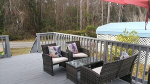 Een terras met rieten meubels en een glazen tafel, omringd door een wit lattenhek.