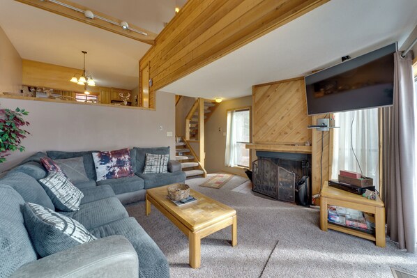 A cozy living room with a sofa, a coffee table, a fireplace, and a TV. - Walk to Lifts: Ski-In/Ski-Out Angel Fire Condo (Angel Fire)