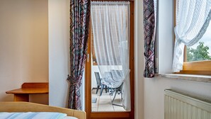 Een slaapkamer met een houten bed, een tafeltje, een stoel en uitzicht door een deur op een terras.