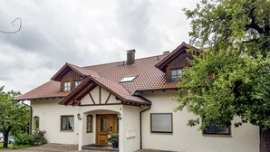 Een twee verdiepingen tellend huis met een pannendak, een houten voordeur en een verharde oprit.