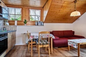 A kitchen with wooden cabinets, a dining table with a floral tablecloth, a red sofa, and a ceiling fan.