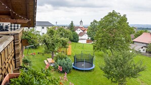 Een achtertuin met een trampoline, speeltoestellen en een uitzicht op huizen en een kerk in de verte.