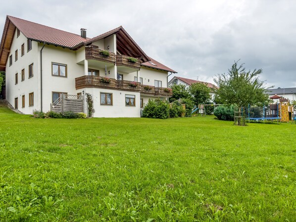 A two-story building with a balcony, a grassy yard, and a playground.