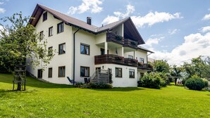Une maison à deux étages avec un balcon, un escalier et une cour gazonnée.