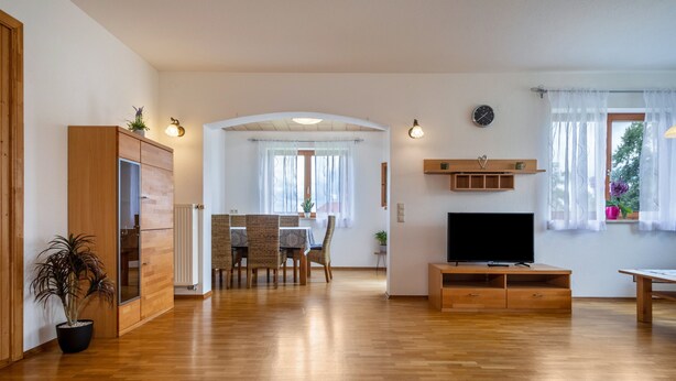 Un vaste espace de vie doté d’un plancher en bois, d’un téléviseur, d’une table à manger avec des chaises, et d’un coin cuisine avec des placards et un réfrigérateur.