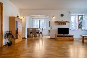 A spacious living area with a wooden floor, a TV, a dining table with chairs, and a kitchen area with cabinets and a refrigerator. - Comfortable vacation apartment 70 m² with private terrace (Gornhofen / Ravensburg)