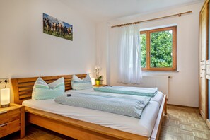 A bedroom with a wooden bed, a bedside table with a lamp, a window with curtains, and a picture on the wall. - Comfortable vacation apartment 70 m² with private terrace (Gornhofen / Ravensburg)