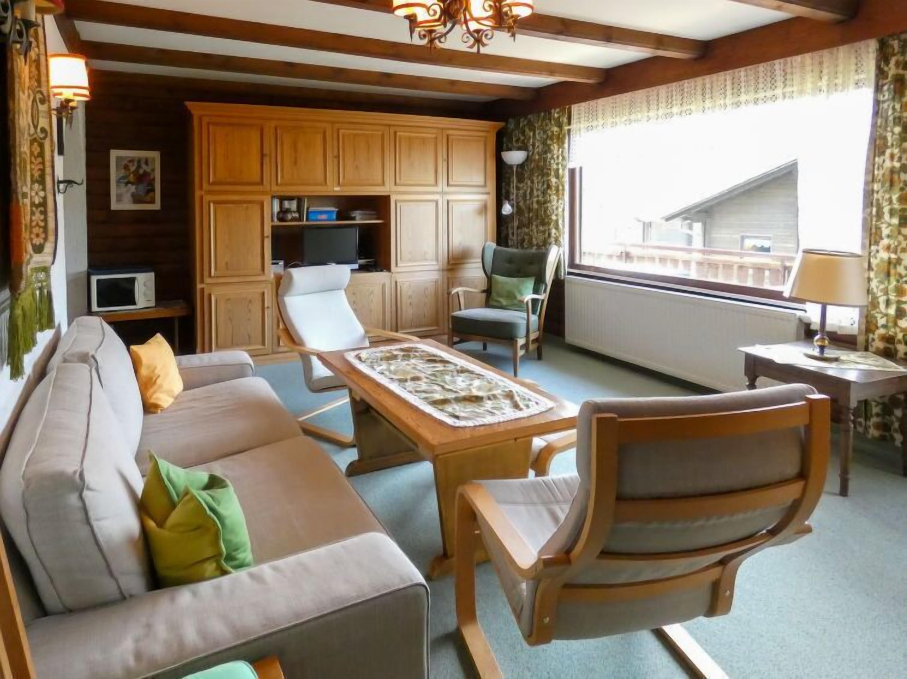 Ein gemütliches Wohnzimmer mit einer Couch, zwei Sesseln, einem Couchtisch, Holzschränken, einem Fernseher und einem Fenster mit Blick.