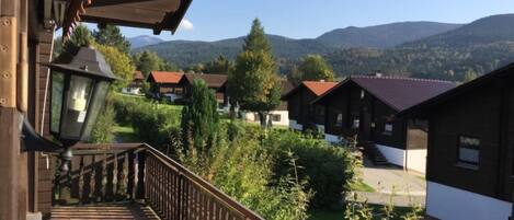 A balcony with a table and chairs, overlooking a village with traditional houses and mountains in the background.