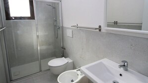 Ein modernes Badezimmer mit einer Duschkabine aus Glas, Toilette, Bidet und Waschbecken mit Holzschrank.
