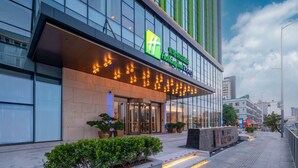 Een Holiday Inn Express gebouw met een glazen gevel, plantenbakken en een goed verlichte entree.