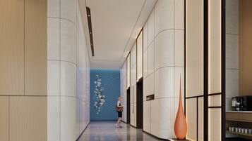 A modern hotel corridor with a woman walking. It features a blue geometric wall, a tall orange vase, and a coffee machine on a counter.