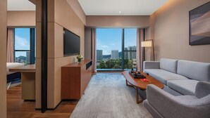 Een moderne hotelkamer met een groot raam met uitzicht op de stad, een flatscreen televisie aan de muur, een bank en een houten bijzettafeltje.