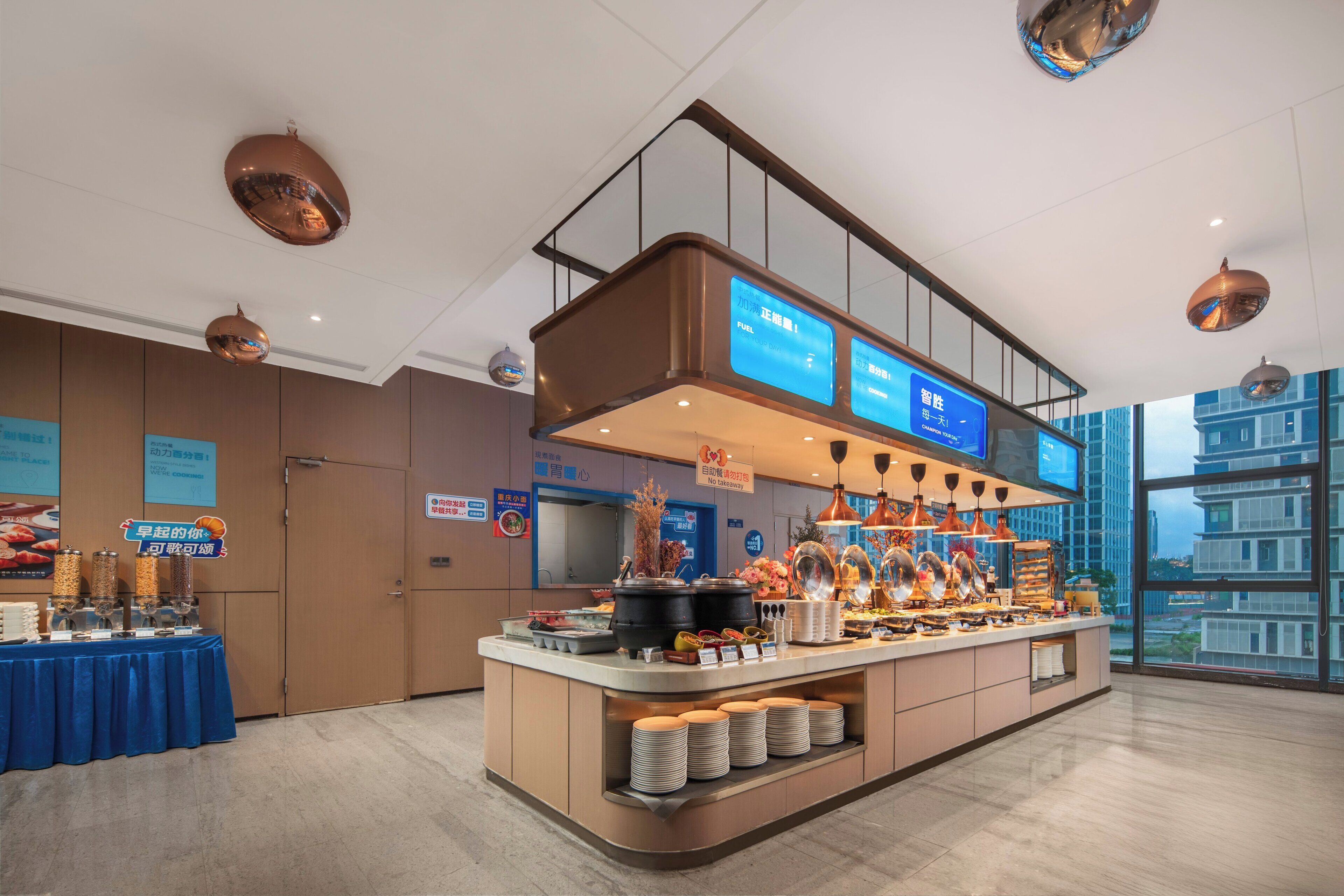 A modern hotel lobby with a buffet area, a reception desk, and a large window offering a city view.