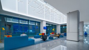Een moderne lobby met blauwe zithoeken, een glazen wand en een plafond met hangende lampen.