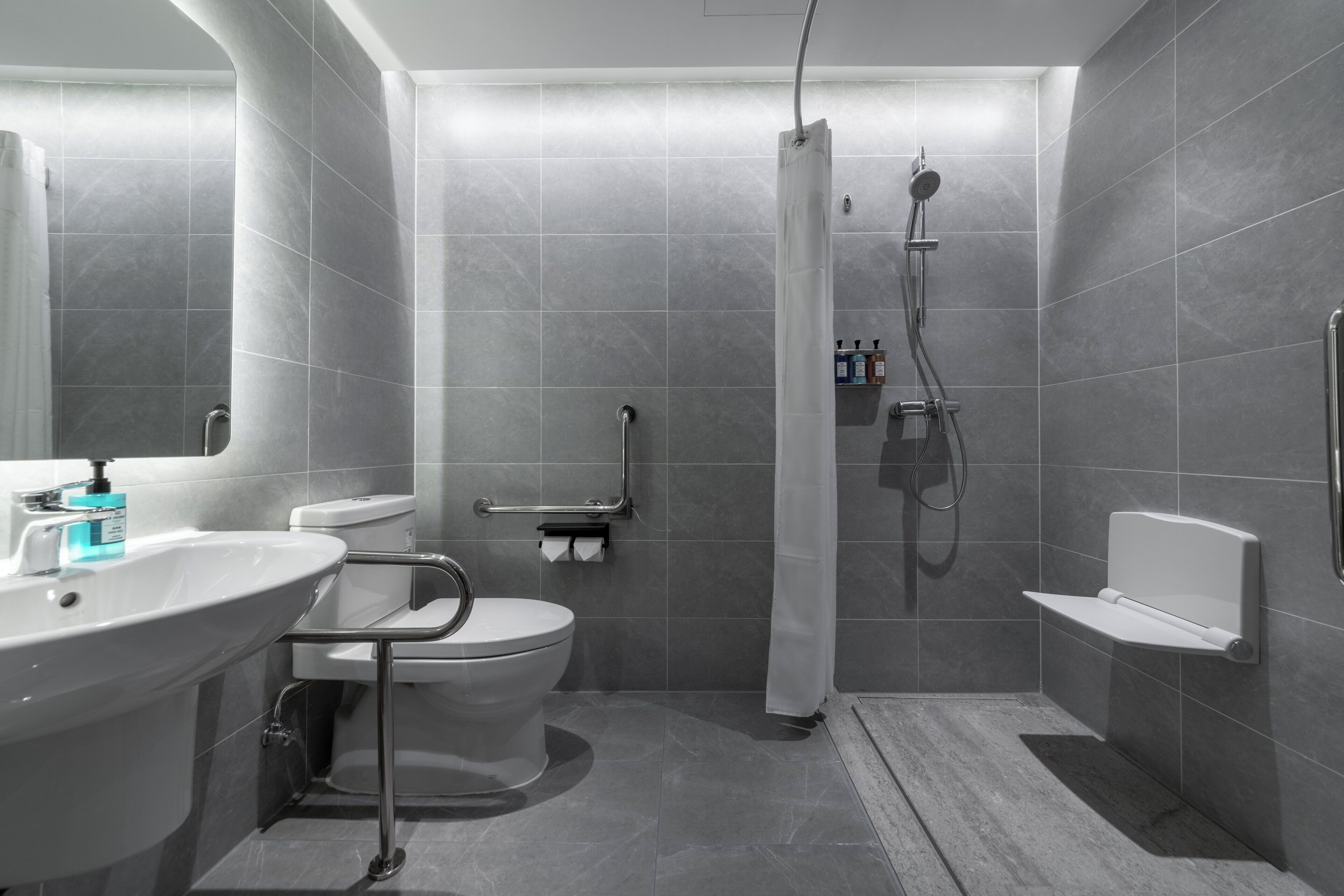 Ein modernes Badezimmer mit Toilette, Waschbecken, Dusche und Haltegriffen.