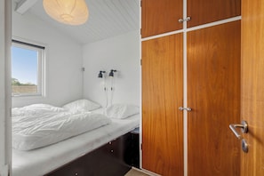 A bedroom with a bed, a wooden wardrobe, and a window.