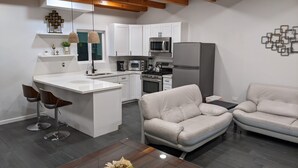 A modern kitchen with white cabinets, a central island, and stainless steel appliances. There are two beige sofas and a wooden coffee table with a vase. - Brand New Studio, Confortable, and gated parking, close to downtown. (Ensenada)