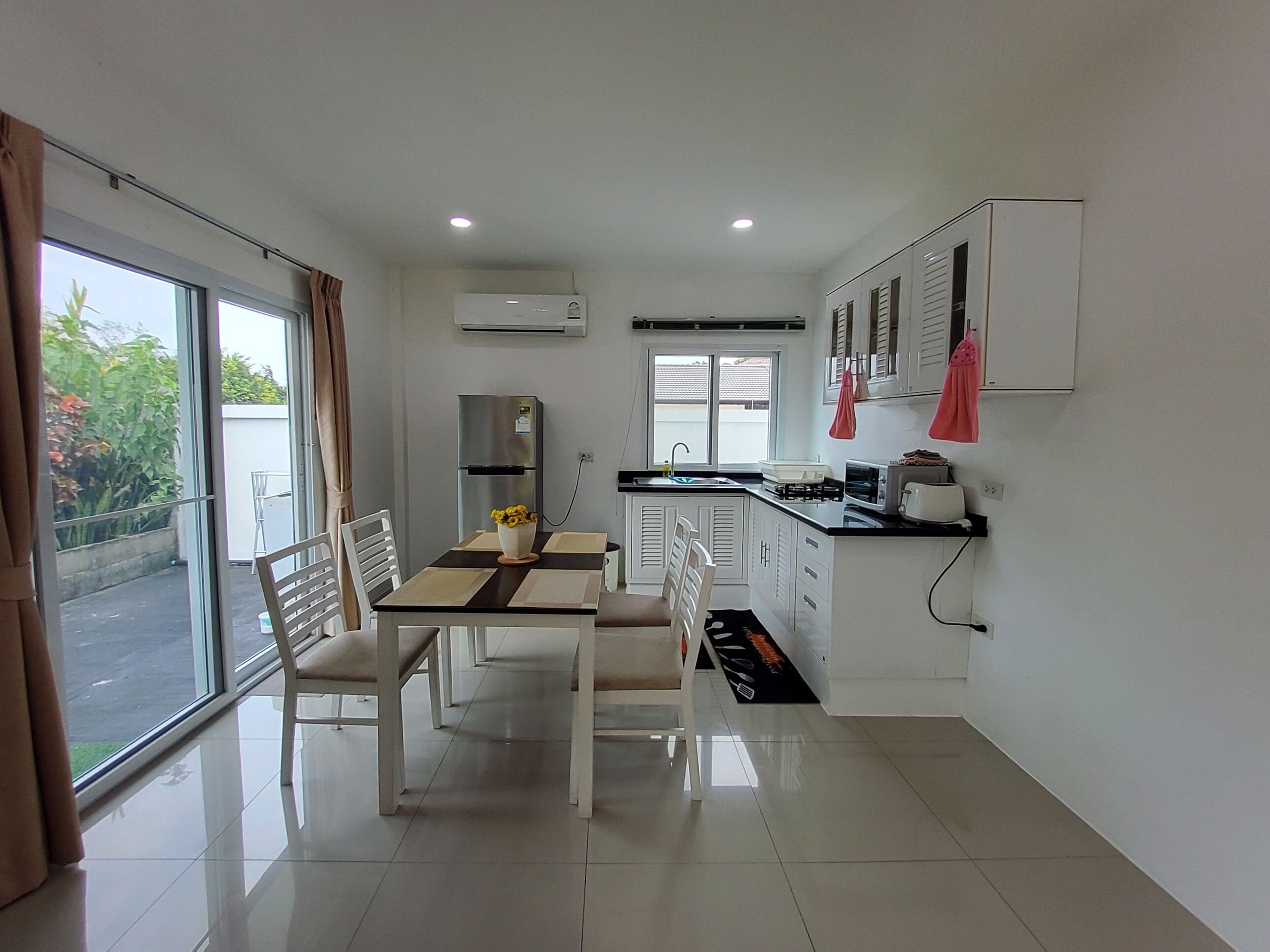 Een moderne keuken met witte kasten, een eettafel met stoelen en een uitzicht door de glazen deur.
