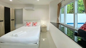 Una habitación de hotel con cama, ventilador de techo, aire acondicionado, mesita de noche, lámpara y ventana con cortinas.