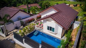 Una casa de dos pisos con piscina, un patio cercado y un techo de tejas rojas.
