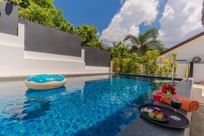 Una piscina azul cristalina con un flotador, una toalla y una bandeja con bebidas y aperitivos.