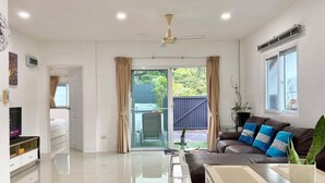 Una sala moderna con un sofá, una mesa de centro y un televisor. Hay un ventanal corredero que da a un área exterior.
