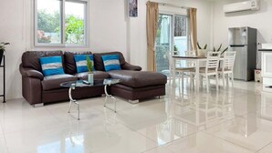 Una sala de estar moderna con un sofá de cuero marrón, una mesa de centro de vidrio y un comedor con sillas blancas y una mesa.