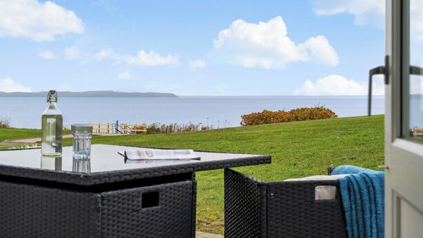A view from a room with a glass door, overlooking a grassy area and a body of water. - Cozy Brenderup Apartment on the Beach (Middelfart)