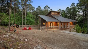 A cabin with a deck, surrounded by trees. - Glorious Sunset - Hot Tub - Fire Pit - Game Room - Forest Views - Sleeps 8 (BROKEN BOW)