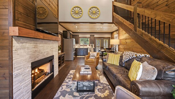 A spacious living area with a fireplace, leather sofa, and a staircase leading to an upper level. - Glorious Sunset - Hot Tub - Fire Pit - Game Room - Forest Views - Sleeps 8 (BROKEN BOW)