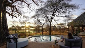 Ein Sitzbereich am Pool mit Blick auf eine natürliche Landschaft und einen Sonnenuntergang.