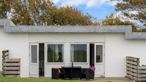 Un bâtiment moderne doté d’un patio comprenant une table et des chaises, de grandes fenêtres et une pelouse verdoyante.