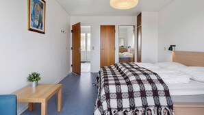 Une chambre moderne avec un grand lit, une table de chevet agrémentée d’une plante, un luminaire suspendu et une porte donnant sur une autre pièce.