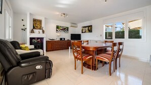 Ein geräumiges Wohnzimmer mit einer schwarzen Ledersofa, einem Esstisch mit sechs Stühlen sowie einer Küchenzeile mit Holzausstattung und einem Fernseher.