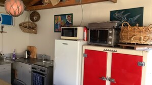 A kitchen with a red refrigerator, a microwave, and a stove. There is a hanging light fixture and a painting on the wall.