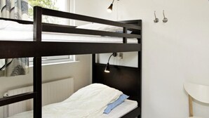 Un lit superposé avec un matelas blanc et un oreiller bleu, une lampe de chevet et une fenêtre avec des stores.