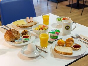 A breakfast table with bread, eggs, pastries, fruit, and juice.
