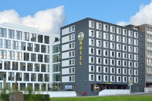 Un bâtiment d’hôtel moderne, avec une grande enseigne « HÔTEL » bien visible sur la façade, caractérisé par une série de fenêtres disposées en réseau et un toit plat.