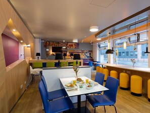 Un espace repas moderne avec une table blanche, des chaises bleues et une fresque colorée sur le mur.