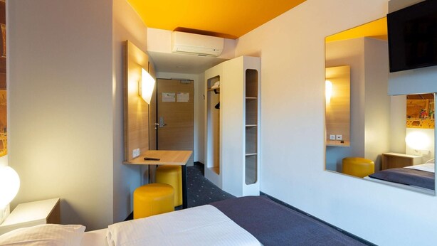 Une chambre d’hôtel équipée d’un lit, d’un bureau, d’une chaise, d’un miroir et d’une télévision.