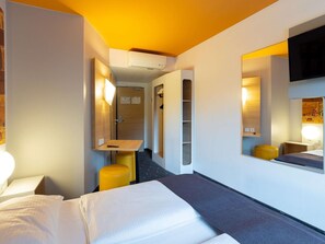 Une chambre d’hôtel équipée d’un lit, d’un bureau, d’une chaise, d’un miroir et d’une télévision.