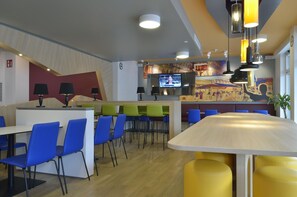 A modern restaurant with a bar area, multiple seating options including tables and chairs, and a television screen displaying a news program.