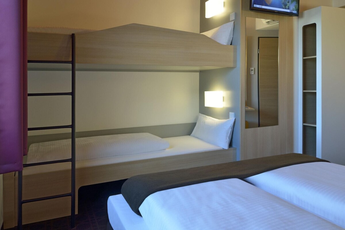 Une chambre avec un lit superposé, un téléviseur fixé au mur, une table de chevet et une armoire.